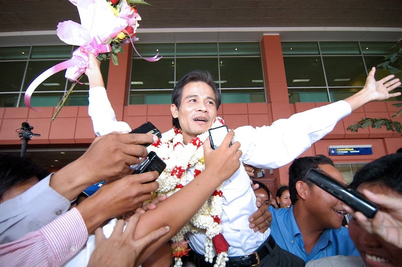 Chea Mony, with flower garlands around his neck , jumps into the air while wearing flower garlands around his neck in front of supporters holding audio recorders.